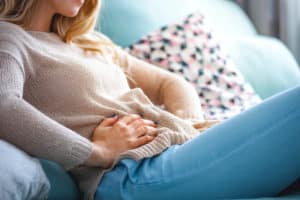 woman sitting on couch holding stomach due to pain, needs abdomen x-ray